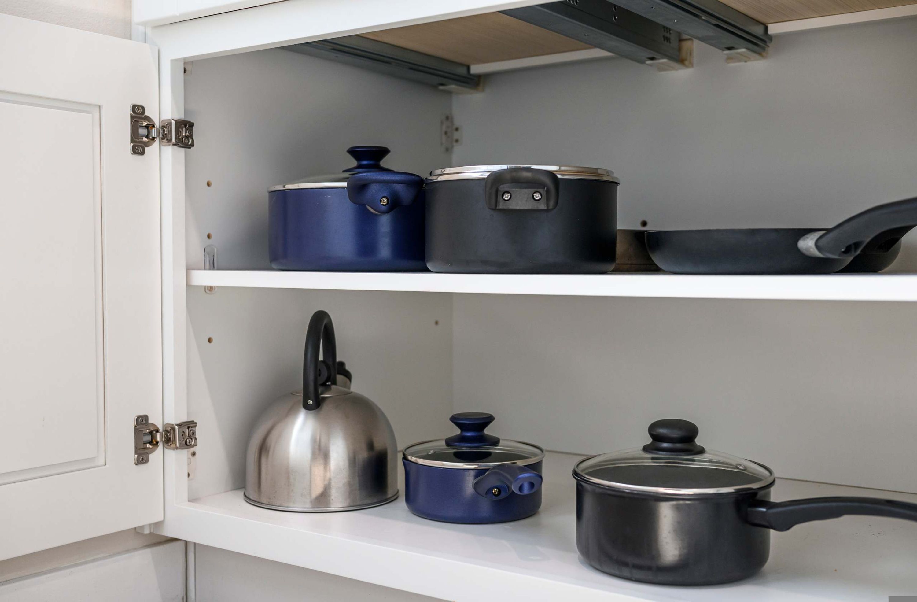 A kitchen with white cabinets and shelves holding various kitchenware, including pots, pans, and a kettle.