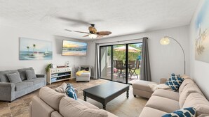 A living room with a sofa, coffee table, and artwork on the walls. - Gulf Highlands escape - pool and beach access (Panama City Beach)