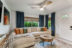 A living room with a sectional sofa, a round coffee table, a ceiling fan, and a large window with curtains. - The Break Tropical Family Oasis Near Beach (Treasure Island)