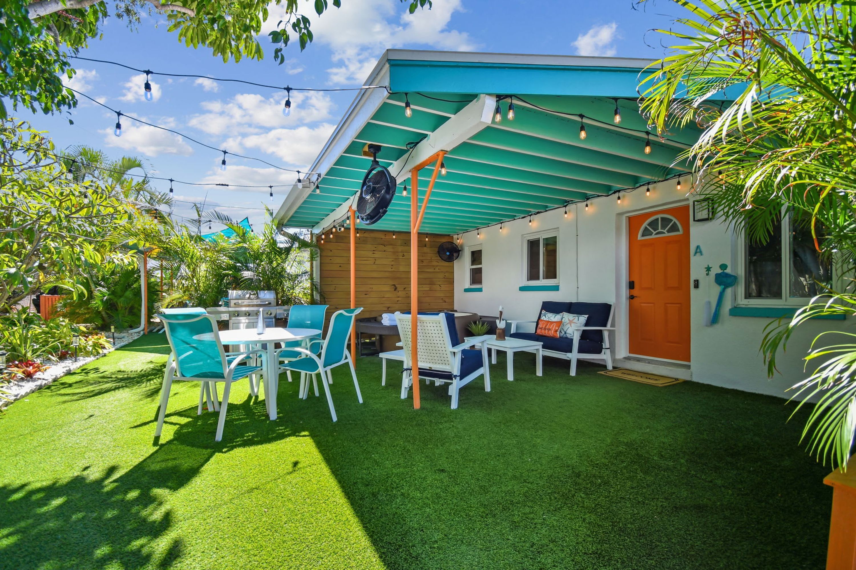 A patio area with a table and chairs, a fan, and a door with an orange frame.