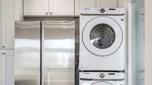Une cuisine compacte dotée d’appareils électroménagers en acier inoxydable, notamment un réfrigérateur, ainsi qu’un lave-linge et un sèche-linge superposés.