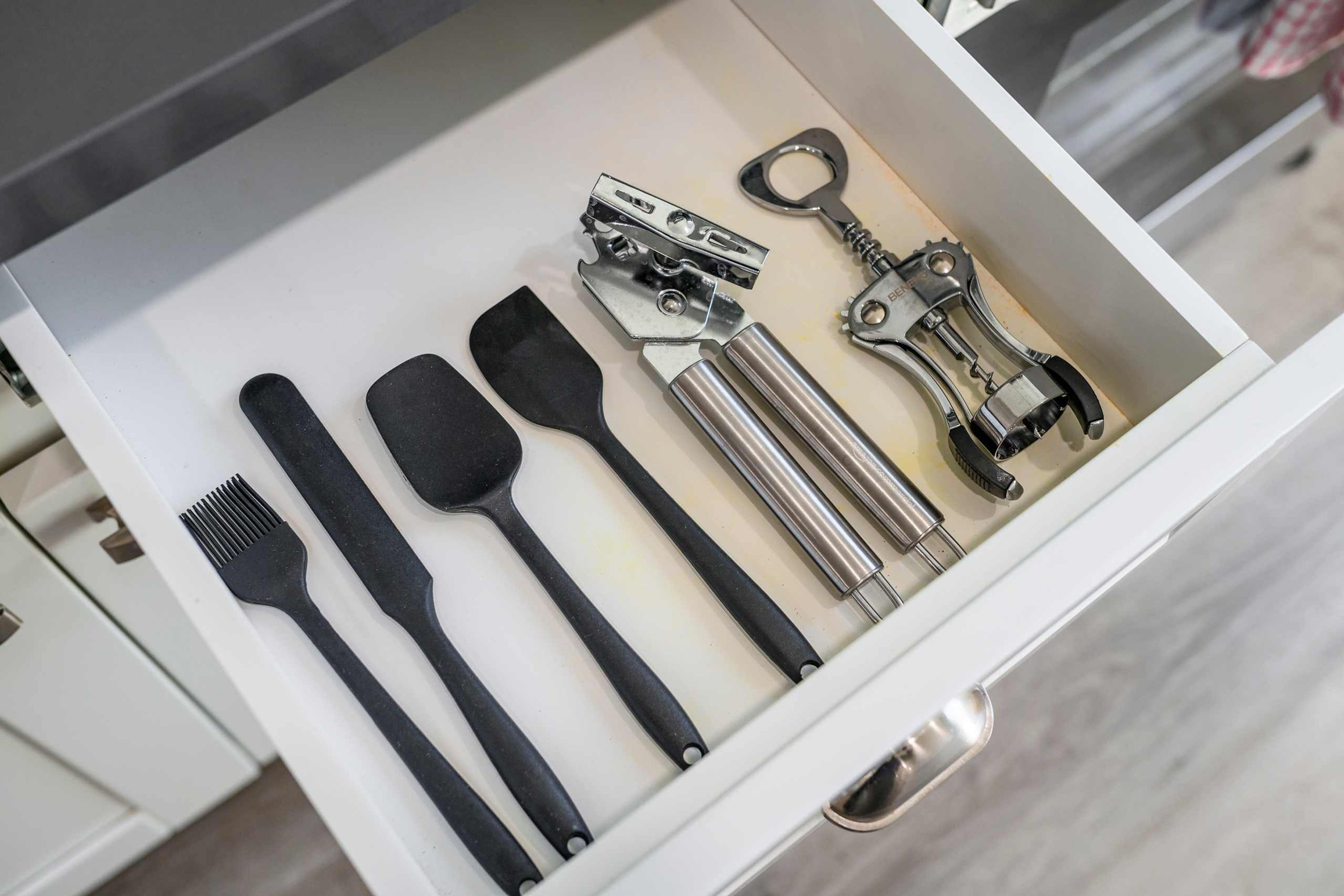 Un tiroir contenant divers ustensiles de cuisine, notamment des spatules, une râpe et un ouvre-boîte.