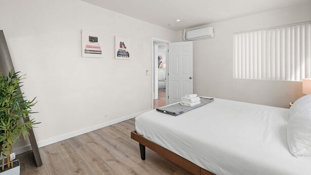 Une chambre d’hôtel moderne avec un lit soigneusement fait, une plante en pot et des œuvres d’art accrochées au mur.