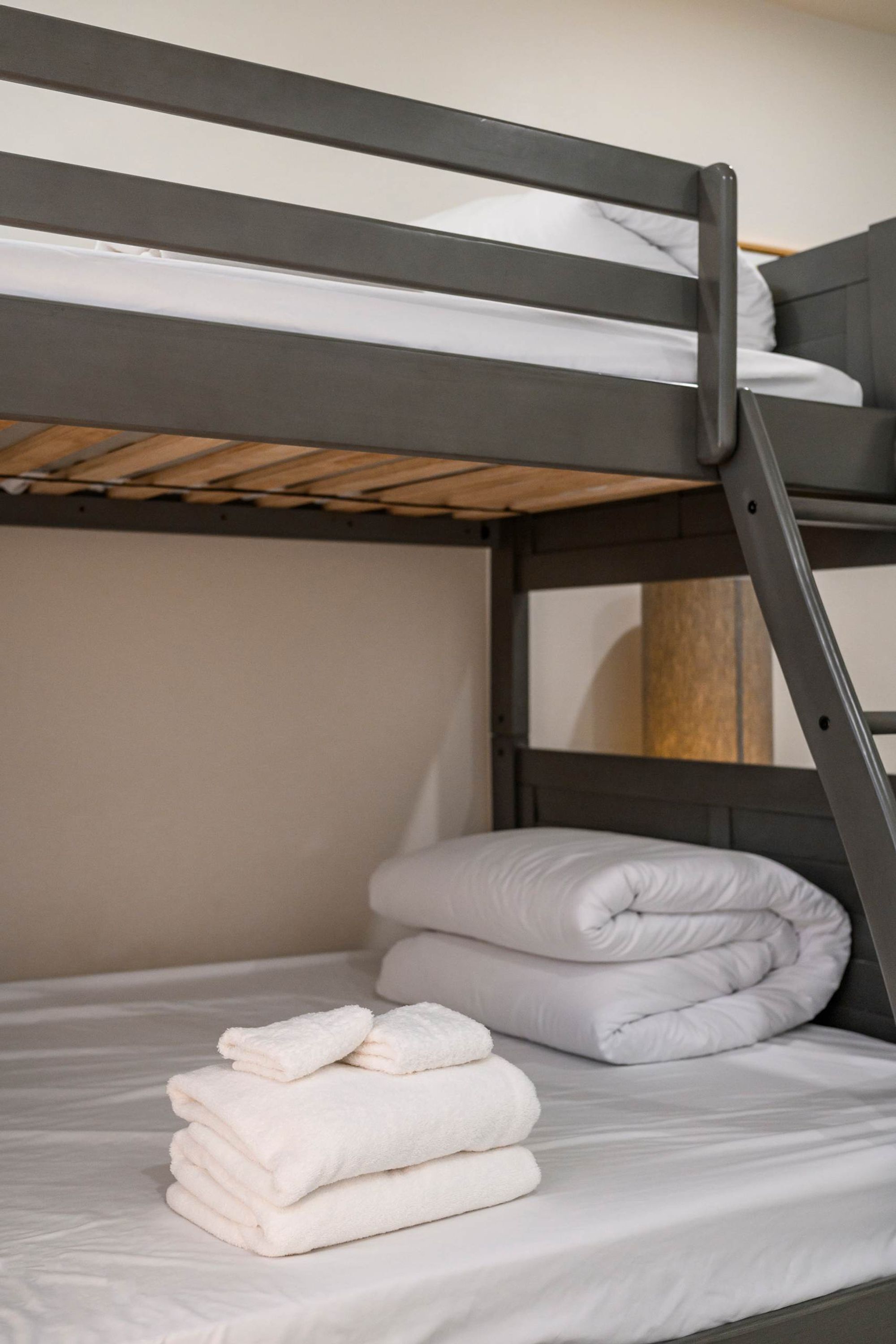 A bunk bed with a wooden ladder, white bedding, and neatly folded towels.