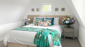 A bedroom with a bed, a nightstand, a window, and a wall-mounted picture frame. - 3 bedroom cottage in Sark, on the Avenue. (Guernsey)