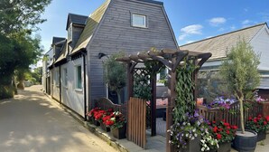 A residential street with a house featuring a wooden pergola with climbing plants and flower beds. - 3 bedroom cottage in Sark, on the Avenue. (Guernsey)
