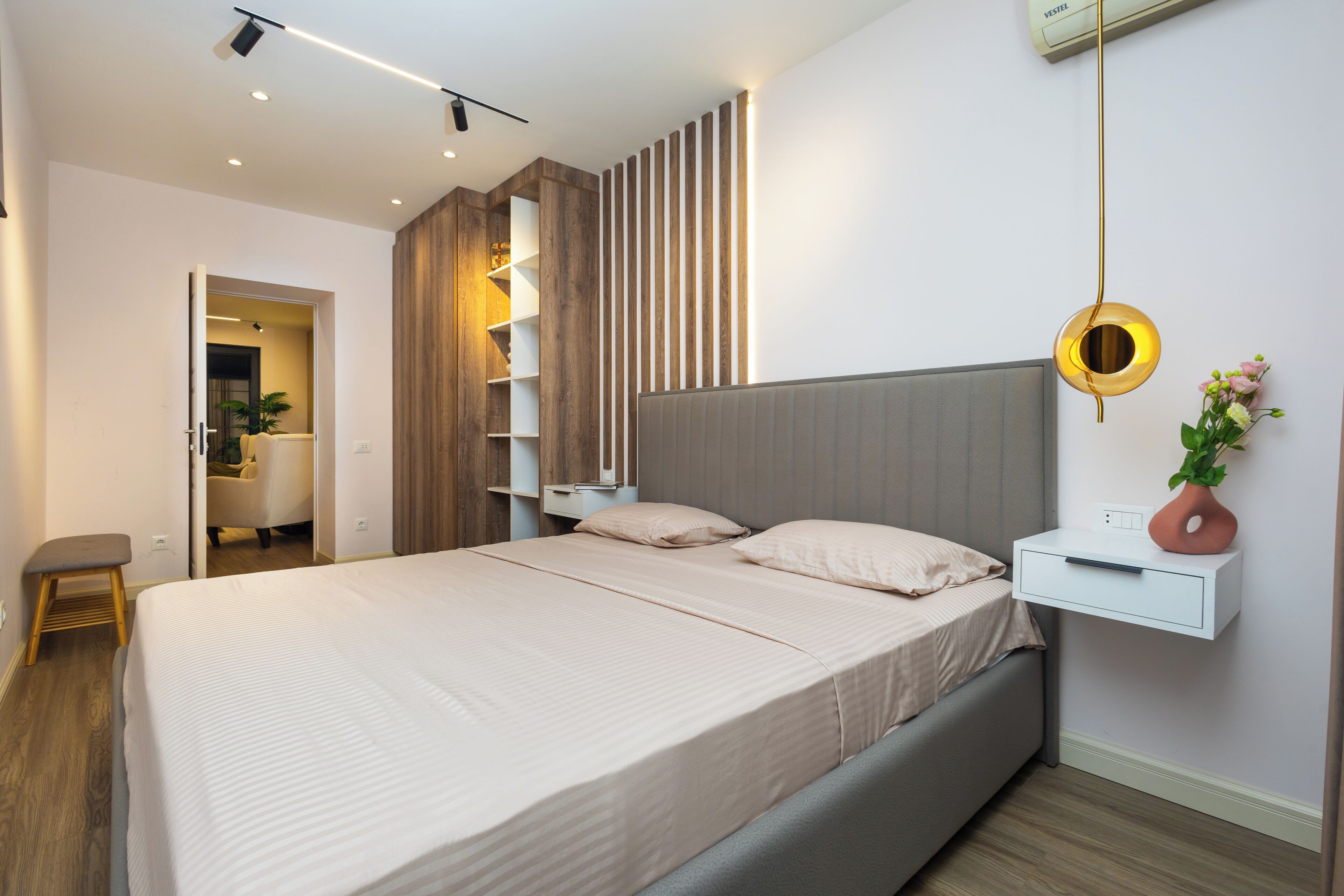 A modern bedroom with a large bed, bedside tables, a wall-mounted shelf, and a hanging light fixture.