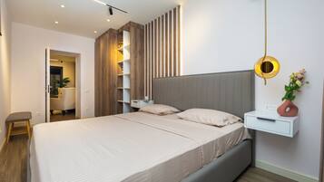 A modern bedroom with a large bed, bedside tables, a wall-mounted shelf, and a hanging light fixture.
