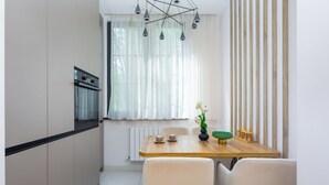A compact kitchen with a built-in oven, a dining table with chairs, and a window with sheer curtains.