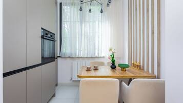 A compact kitchen with a built-in oven, a dining table with chairs, and a window with sheer curtains.