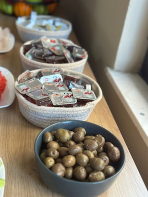 A table with bowls containing various food items, including packaged snacks and olives. - Rumar Hotel (Durres)