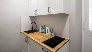 A compact kitchenette with a black induction cooktop, a sink with a faucet, and a kettle. There are two bottles of Pellegrino water and a coffee maker on the counter.