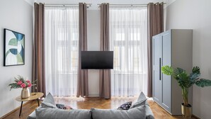 A living room with a grey sofa, a flat-screen TV, a cabinet, and a potted plant.