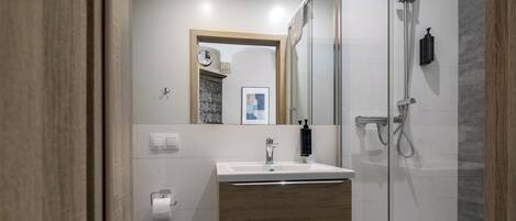 Une salle de bain moderne avec une douche à l’italienne en verre, un lavabo avec un meuble-vasque en bois et un miroir au-dessus du meuble-vasque.