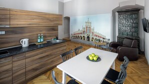 A modern kitchen with wooden cabinets, a white dining table with chairs, and a painting of a building on the wall.
