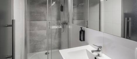 Ein modernes Badezimmer mit einer gläsernen Duschkabine, einem weißen Waschbecken und einem großen Spiegel.