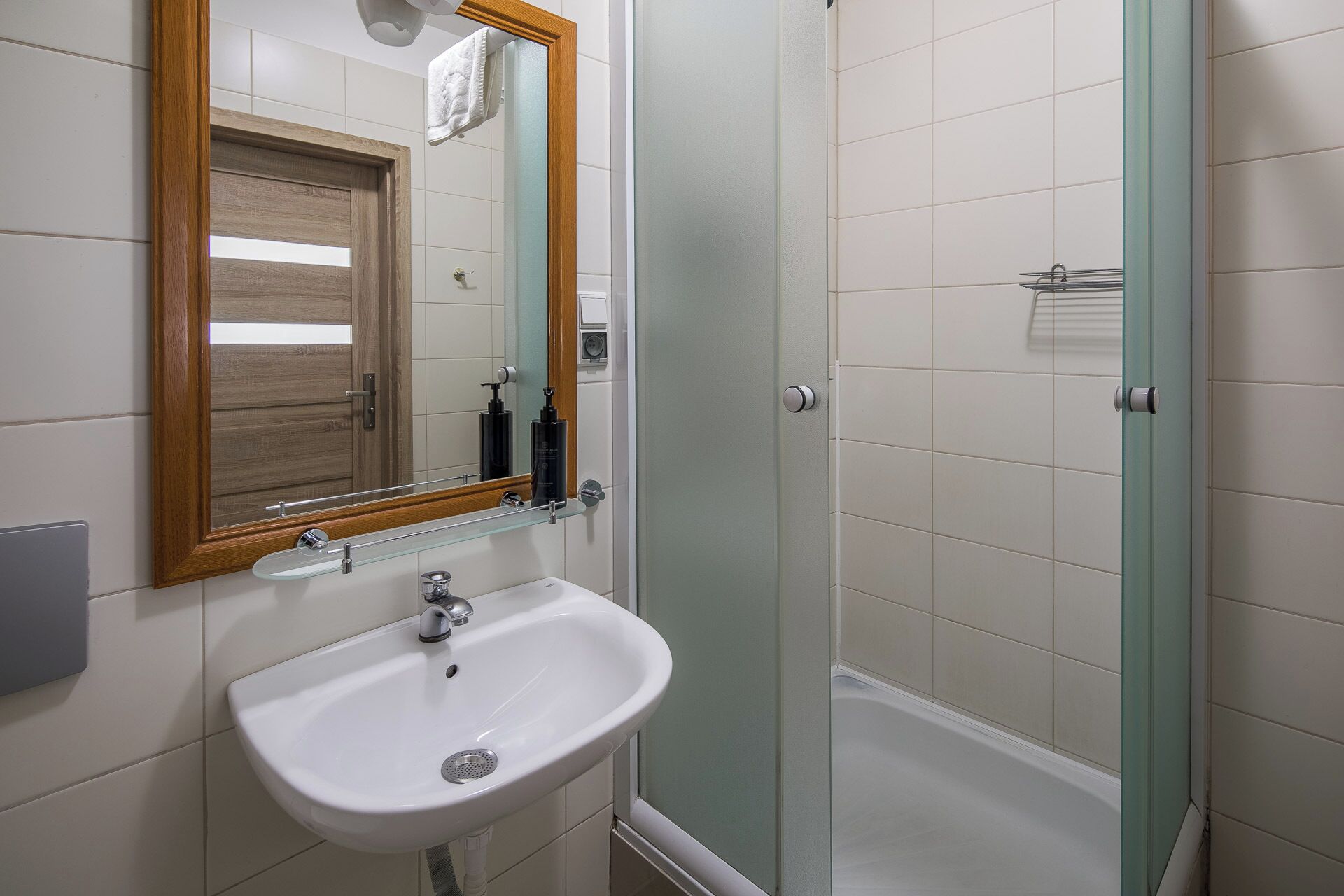 A bathroom with a white sink, a mirror with a wooden frame, a glass shower enclosure, and a towel hanging on the wall.