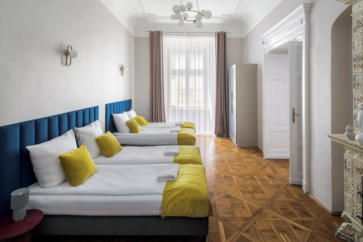 A hotel room with two beds, a wooden parquet floor, a white door, and a chandelier.