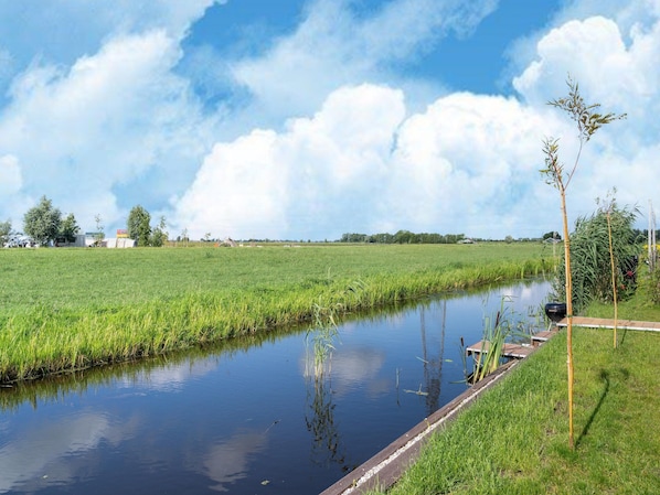 Une rivière paisible aux rives verdoyantes, un ciel dégagé et des arbres qui se dessinent à l’horizon.