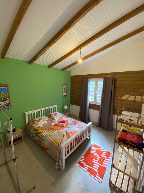 Une chambre à coucher avec un lit, une tête de lit en bois, une table de chevet, une lampe, une fenêtre avec des rideaux, une étagère en bois et un tapis rouge.