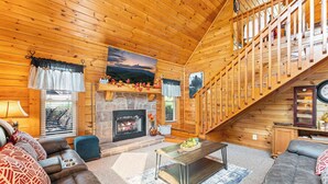 L’intérieur d’un chalet confortable, avec une cheminée, un escalier en bois et un canapé.