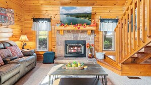 L’intérieur d’une cabane en rondins, avec une cheminée, un canapé, une table basse et un tableau représentant un paysage.