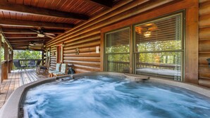 Une cabane en bois dotée d’un bain à remous, d’une terrasse en bois et de grandes fenêtres.