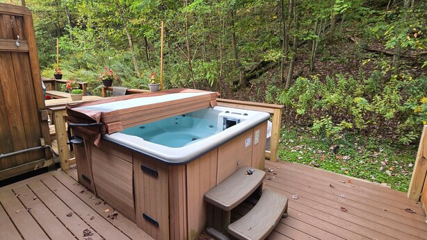Un bain à remous sur une terrasse en bois, entouré de verdure.