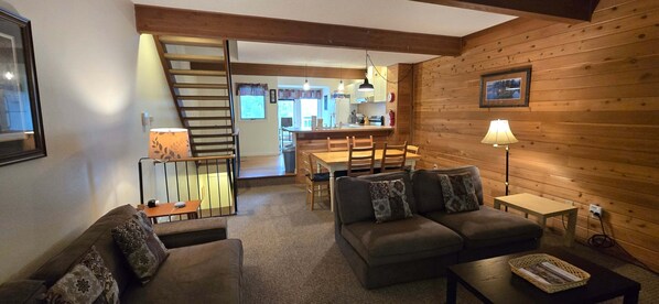 Un salon chaleureux avec un canapé, une table basse, une lampe et un escalier menant à la cuisine.