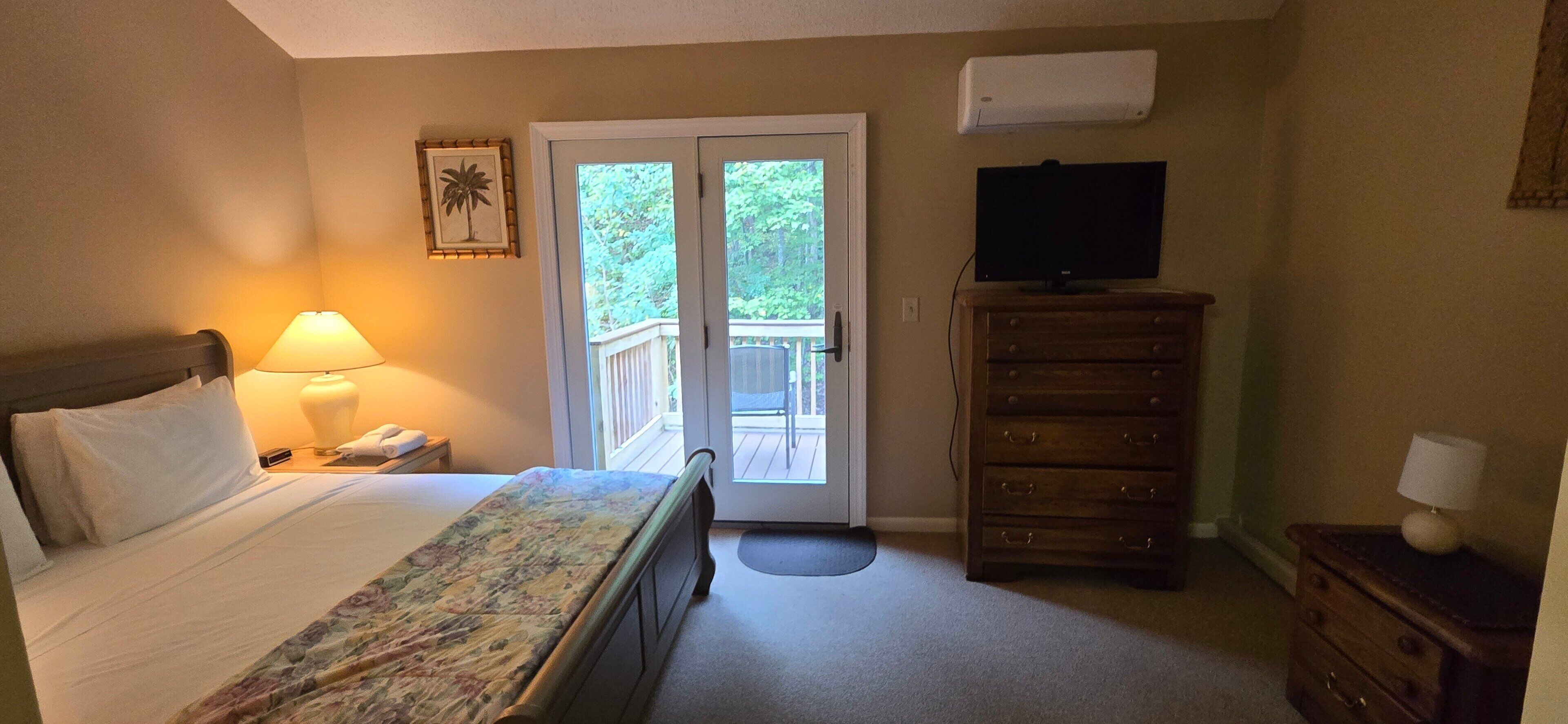 A hotel room with a bed, a nightstand, a lamp, a dresser, a television, and a sliding glass door to a balcony.