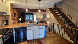 Une cuisine dotée d’un îlot central, d’un lave-vaisselle, d’une cuisinière et d’un évier. Un escalier en bois mène à un autre niveau.