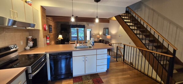 Une cuisine dotée d’un îlot central, d’un lave-vaisselle, d’une cuisinière et d’un évier. Un escalier en bois mène à un autre niveau.