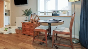 Un salon chaleureux avec un plancher en bois, une table ronde, deux chaises, un téléviseur, une fenêtre donnant sur un beau paysage et une lampe.