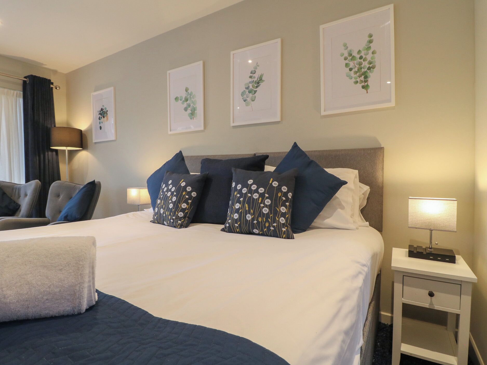 A hotel room with a large bed, two bedside tables, a chair, and artwork on the wall.