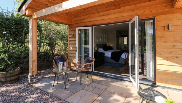 Une cabane en bois avec une porte en verre donnant sur une chambre. Dehors, on trouve deux fauteuils en osier et une petite table.