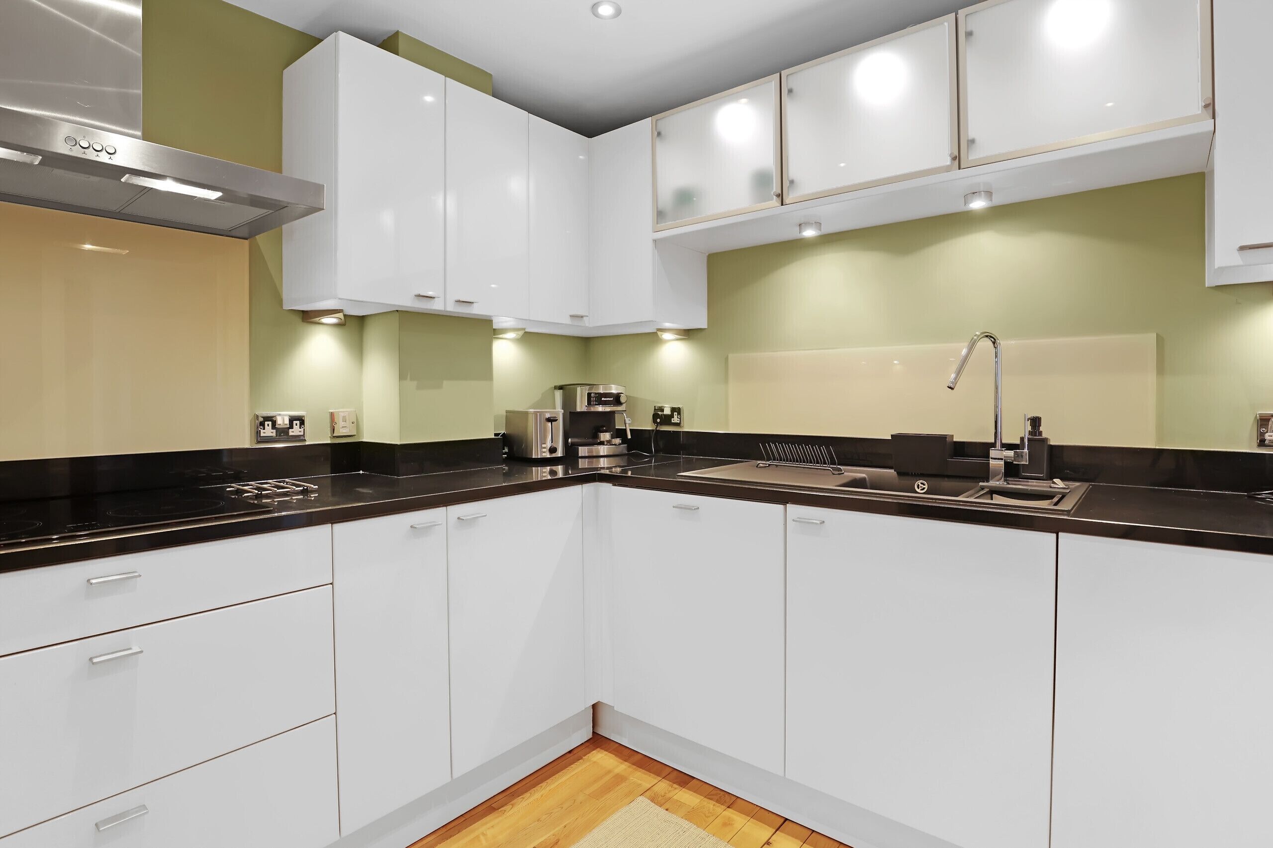 A modern kitchen with white cabinets, a black countertop, and a stainless steel range hood.