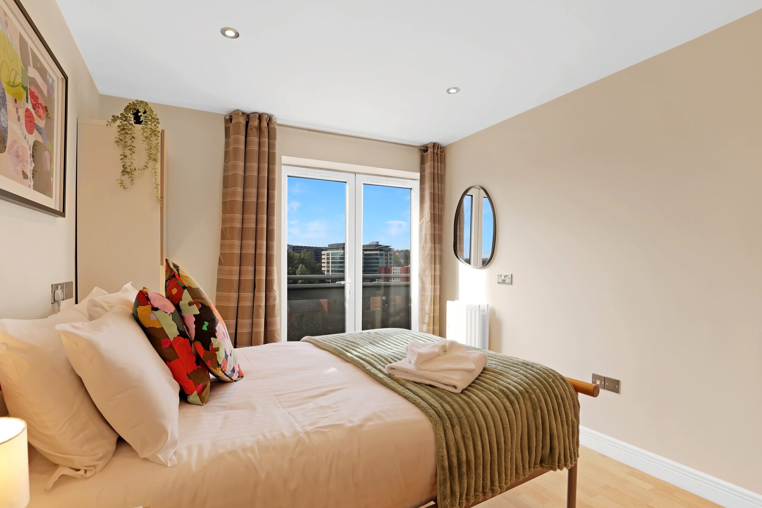 A bedroom with a bed, pillows, a window with curtains, a radiator, and a wall-mounted mirror.