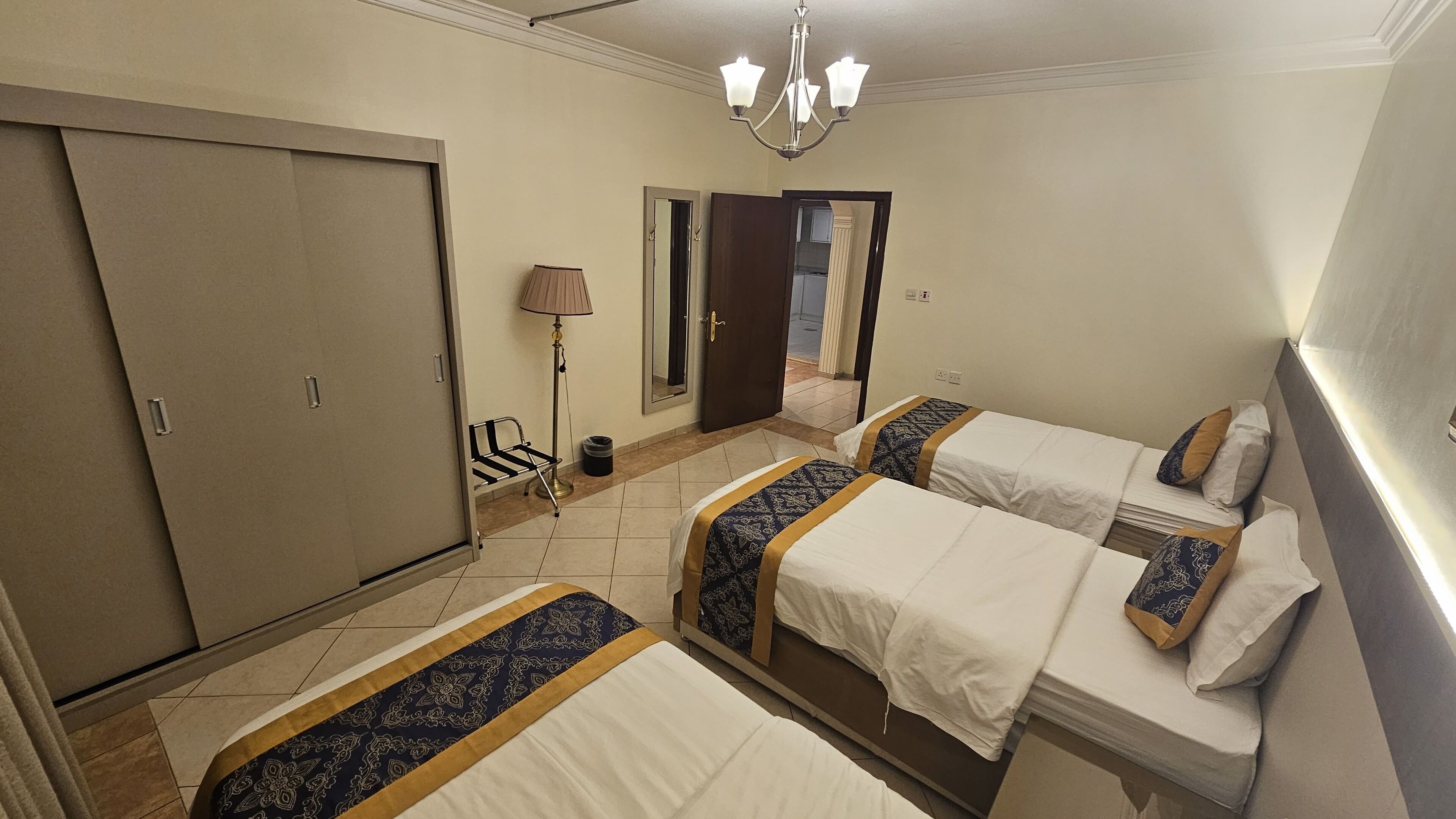 A hotel room with two beds, a wardrobe, a mirror, a lamp, and a chandelier.