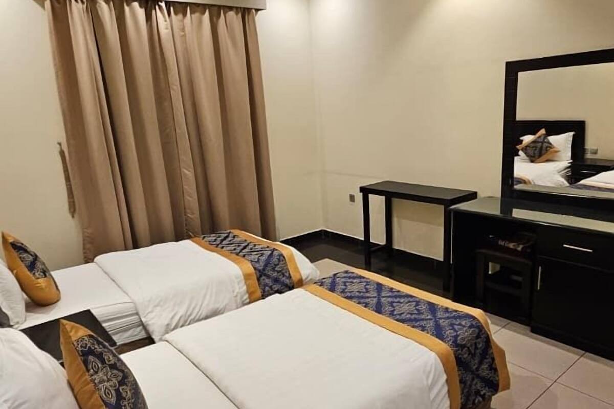 Une chambre d’hôtel avec deux lits, un bureau, une chaise et un grand miroir.
