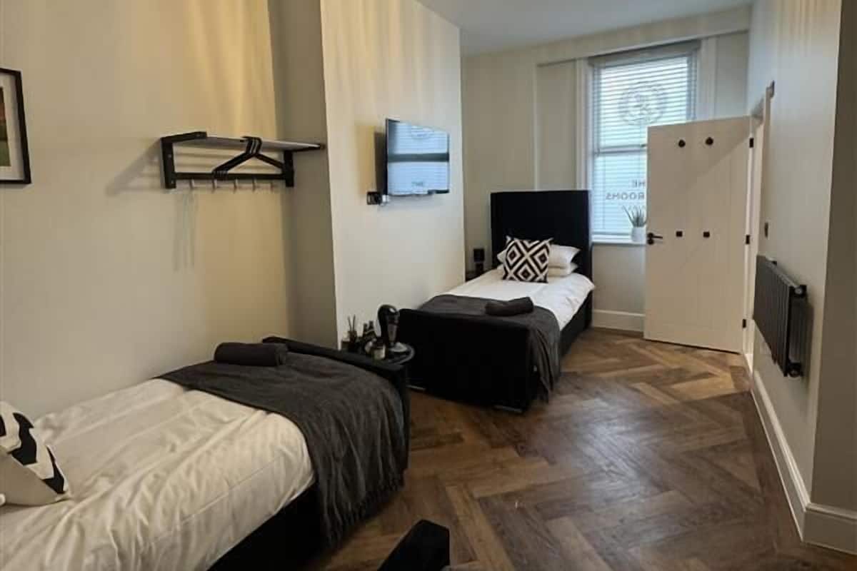 A modern hotel room with two beds, a flat-screen TV, a radiator, and a window with blinds.