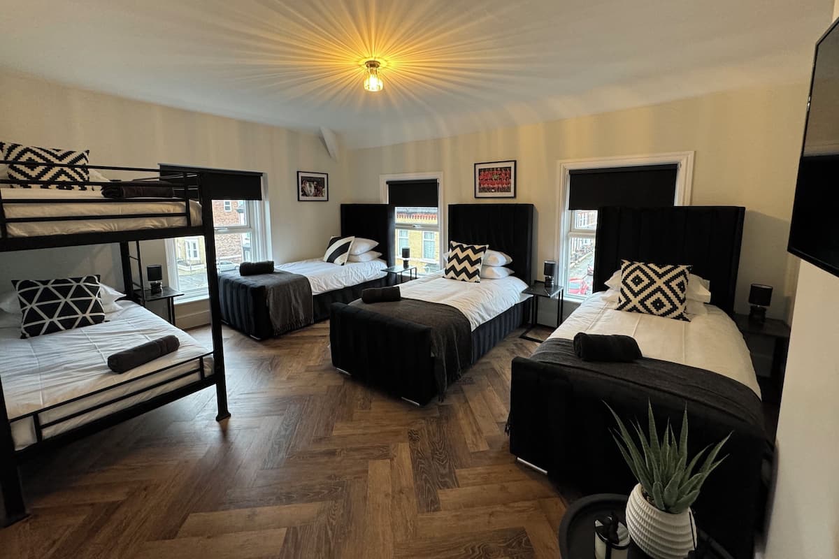 A hotel room with bunk beds, two single beds, a ceiling light, and a potted plant.