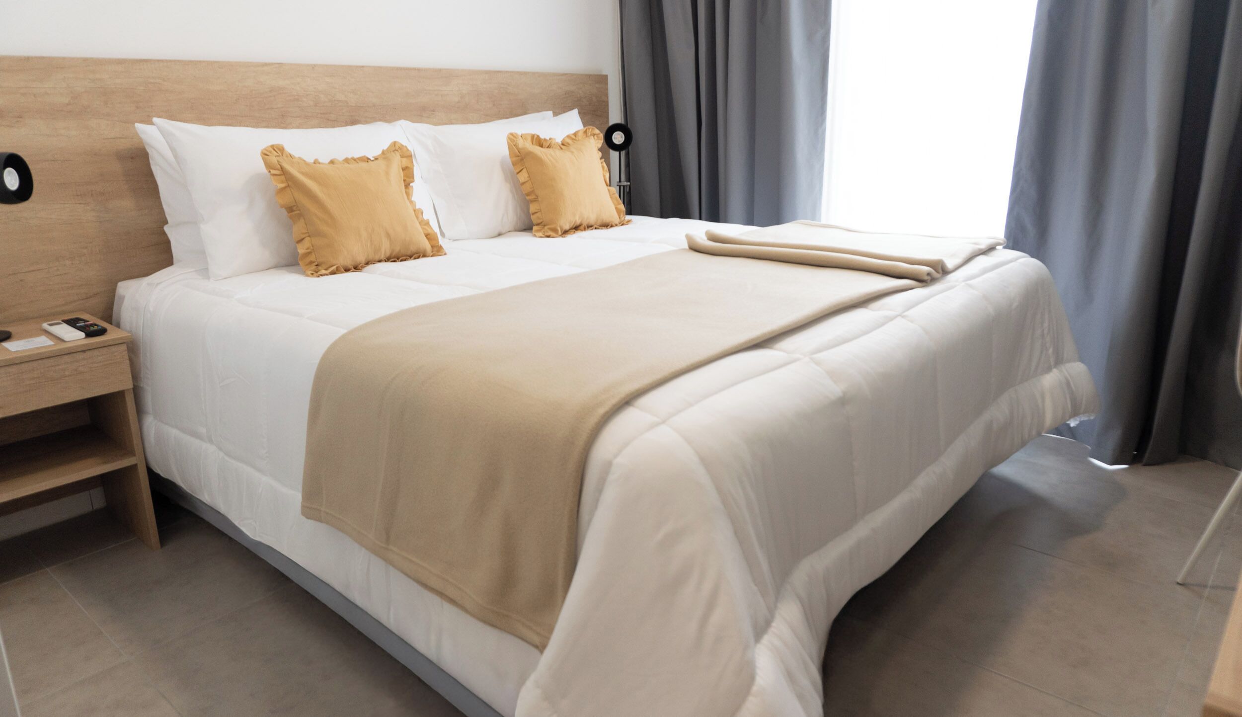 A neatly made bed with a beige blanket, white pillows, and a wooden headboard.