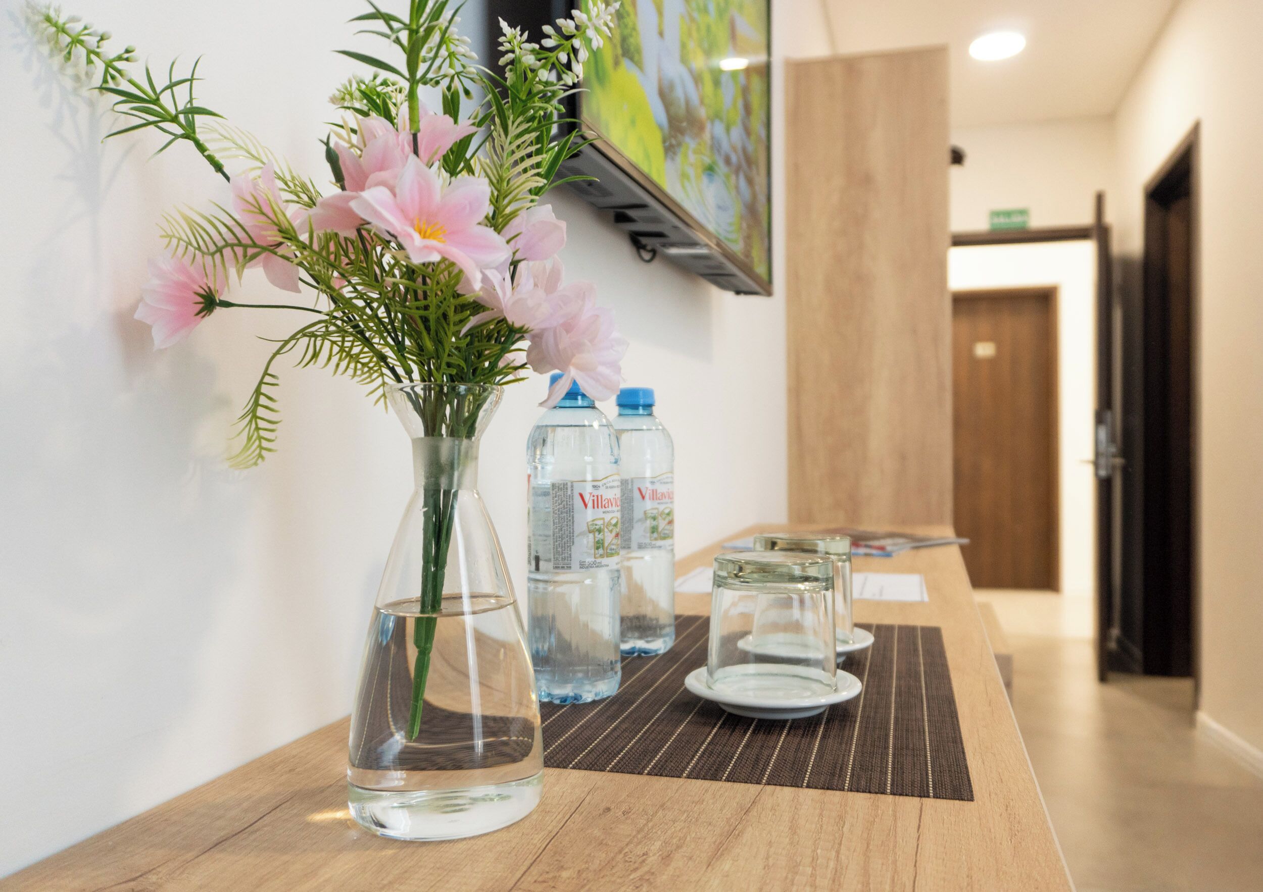 A reception desk with a vase of pink flowers, two water bottles, and a glass on a wooden surface.