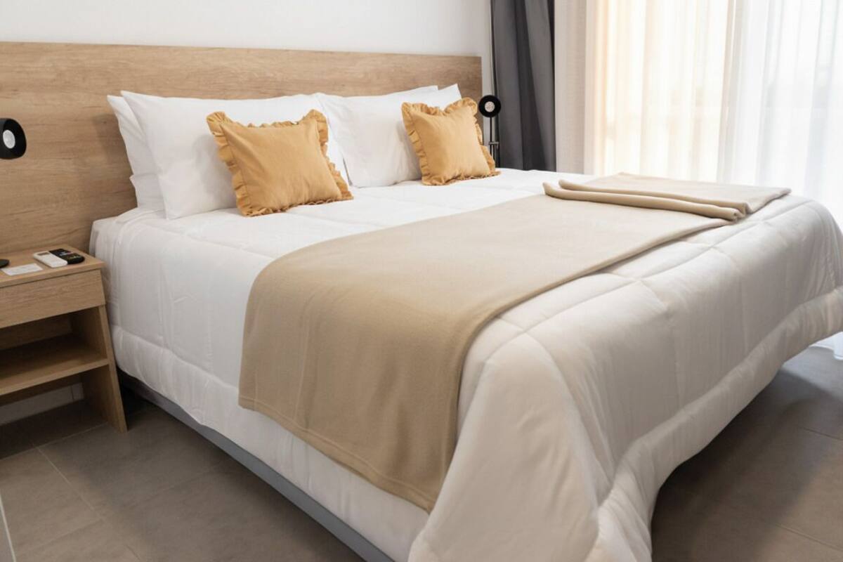 Una cama bien hecha con tablero de madera, dos almohadas y una manta color beige.