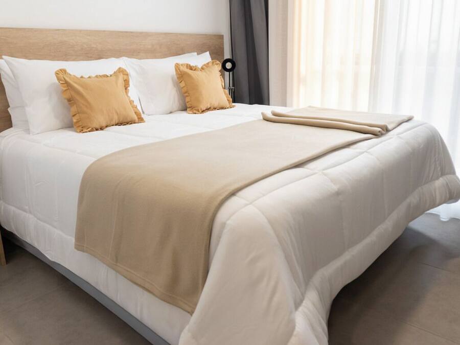 Een net opgemaakt bed met een houten hoofdbord, twee kussens en een beige deken.