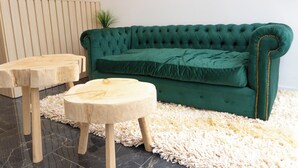 A green tufted sofa with a wooden side table and a smaller round wooden table in a modern room with a shaggy white rug. - RM Campana Hotel (Campana)