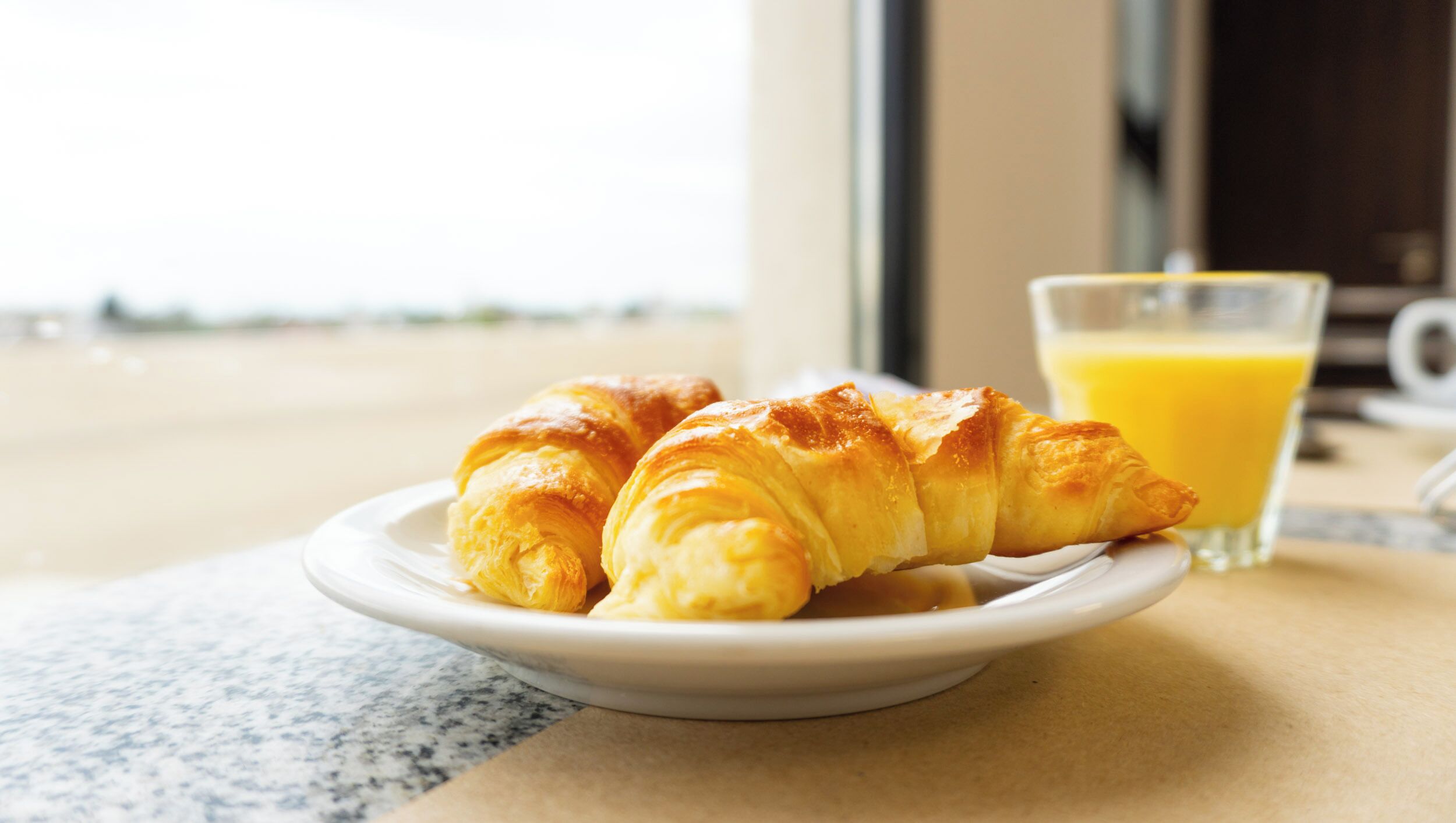 Un plato con croissants y un vaso de jugo de naranja sobre una mesa.