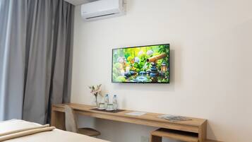 Une chambre d’hôtel avec un lit, un bureau avec un ordinateur, un téléviseur fixé au mur et une fenêtre avec des rideaux.