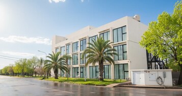 Un edificio moderno con varios pisos, amplias ventanas y un pequeño espacio exterior con palmeras.