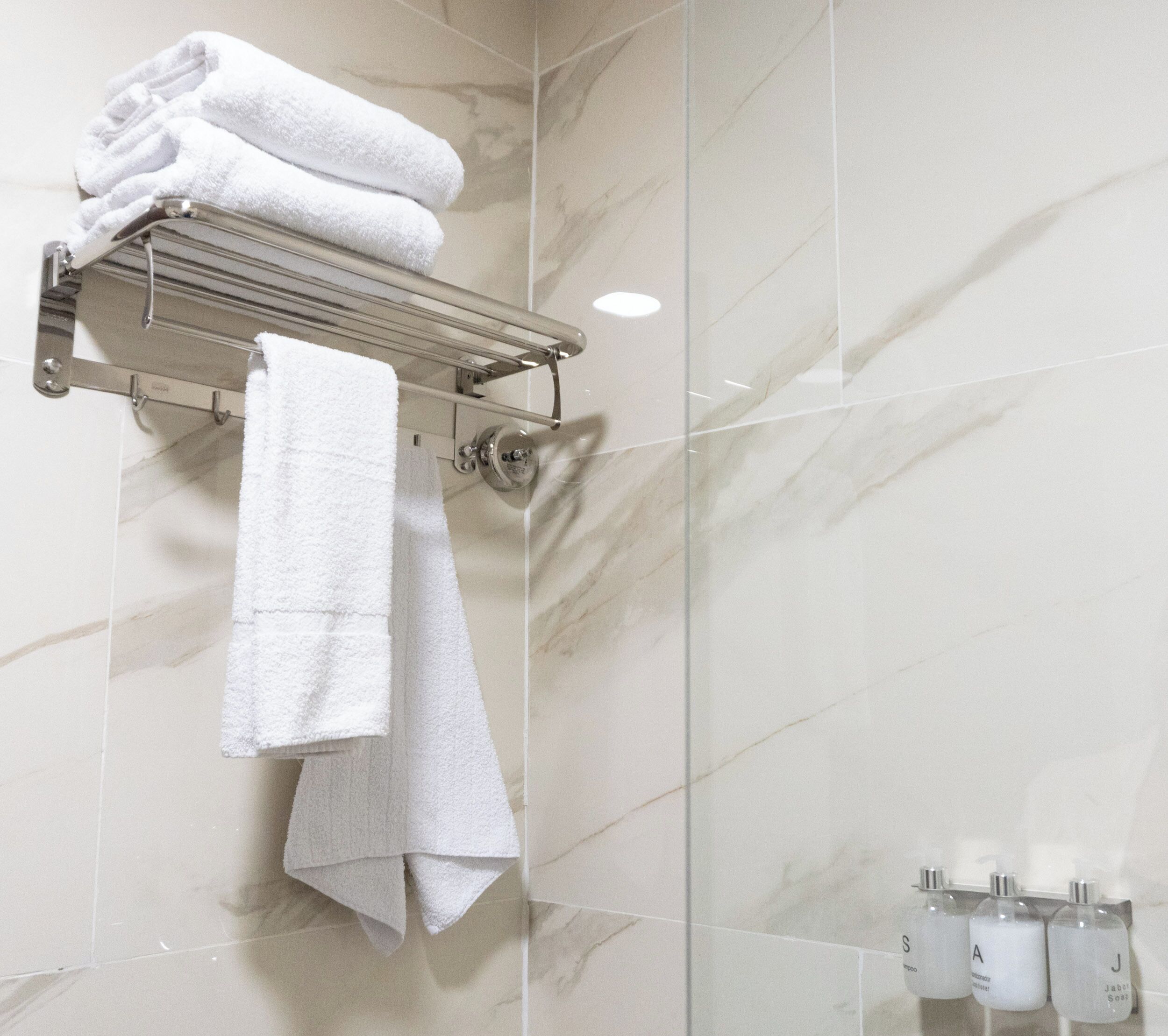 A bathroom with a marble wall, a towel rack with folded towels, and a soap dispenser.